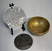 Silver-tone metal disk with engraved face and wings, cast bronze Buddha disk, and a group of the brass bowls.