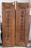 Front view of two solid wood antique doors with carved Chinese characters in vertical panels.