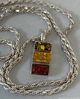Close-up of the multicolor amber and silver necklace showing the pendant stone colors and chain.