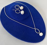 Set displayed on blue stand showing necklace and earrings together to highlight design and size.