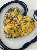 Close-up of the gold-tone and black heart-shaped pendant showing detailed scroll pattern.