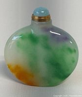 Front view of small oval jade perfume/snuff bottle showing green, orange, and purple natural jade colors and blue stone stopper with gold collar.