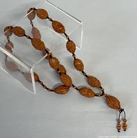 Full view of the carved nut prayer bead necklace displayed on clear acrylic stand, showing the complete length and bead arrangement.