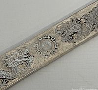 Close-up image of two detailed dragons facing a flaming pearl on a silver bar surface showing intricate engraving and texture.