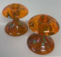 Pair of orange hand blown art glass candle holders with flared base and rounded tops featuring multicolored red and green spots, shown side by side.