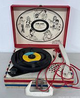 Open view of Dejay portable record player in working condition with a record on the turntable and detailed illustrated lid interior.