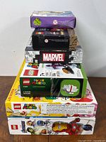 Stack of LEGO boxes showing Marvel, Super Mario, and Avengers themes with visible logos and minor box wear.