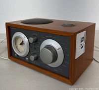 Three angled views of the Tivoli Audio Model Three BT clock radio showing wooden cabinet, front panel with analog clock, control knobs, and speaker grille on top.