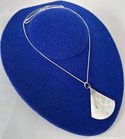 Silver chain necklace with fan-shaped mother of pearl pendant displayed on blue felt stand.