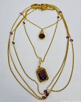 Full view of the 5 strand gold-tone necklace highlighting the layered chains and purple glass or stone beads.
