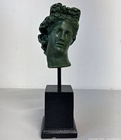 Full front view of the Medusa head statue on its black base against a neutral background.