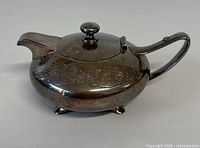 Side view of vintage Rosenthal silver plated teapot showing oval shape, engraved floral scroll design, hinged lid with knob, spout and handle.