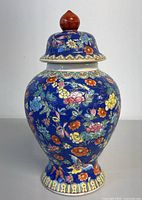 Front view of ceramic ginger jar with vibrant floral hand paint on blue background and domed lid.
