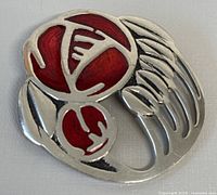 Front view of the pewter brooch showing red enamel floral design with petals and leaves, approximately 2.5 inches wide.