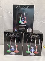 Three boxed sets of Crystolight lighted wine glasses, showing front and side views of packaging with images of glowing wine glasses in green, blue, and red light.