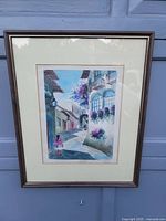 Front view of the framed watercolor painting showing the narrow street, balconies, flowers, and a pedestrian.