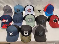 Full lot of 12 baseball caps laid out on a white surface, showing variety of colors and logos.
