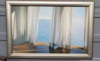 Full view of framed painting showing sheer white curtains with ocean view and wooden floor.
