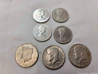 Seven coins: three Kennedy Half Dollars dated 1967 and 1971, four Canadian coins with Queen Elizabeth II portrait and royal crest.