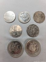 Seven coins displayed on flat surface, including various Australian and Canadian coins: circular and dodecagonal shapes. Two coins sealed in protective cases.