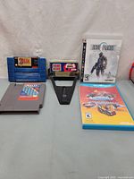 Shows the lot of video game items including The Legend of Zelda SNES cartridge, NES Jeopardy cartridge, Game Genie enhancer, PS3 Lost Planet game case, Wii U game case Emergency Mayhem.