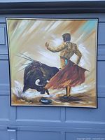 Full view of the framed painting showing the matador facing the bull, light strokes and paint drops visible on surface.