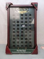 Front view of the display case showing protective corner packaging and closed glass door with slots for 50 coin quarters.