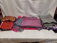 Assorted folded fabrics including patterned and colorful pieces displayed on a white surface.