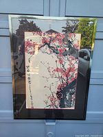 Full view of framed Chinese hanging scroll painting showing plum blossom branches with vibrant red flowers and black calligraphy under glass with gold frame and black matting.