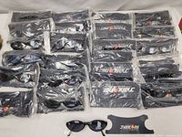 Top-down view of 16 sealed plastic bags each containing one pair of Jianlong sunglasses and one black Jianlong-branded pouch arranged in a grid.
