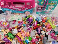 Overview of assorted Shopkins figures, a pink and teal camper van playset, and many small toys and accessories spread on a surface.