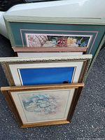 Photo showing four stacked framed pictures leaning against each other, visible frames show green, detailed gold, and simpler gold-toned frames with floral prints.