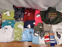 Multiple men's new with tags shirts and socks laid out showing various colors and brands, including Lacoste, Calvin Klein, Dickies, Adidas, and Bluenotes.