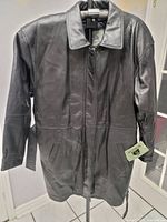 Front view of a new long black leather jacket with pockets and collar, showing attached tag.
