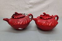 Front view of both red cinnabar lacquer teapots showing carved leaf motifs and lid decorations