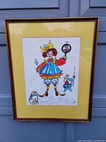 Full view of framed art print showing clown figure standing on cobblestone ground, with a yellow matte and brown frame.
