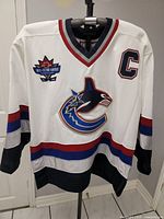 Front view of white Vancouver Canucks hockey jersey with large orca logo, All-Star Game patch, number 11 and captain C patch.