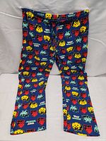 Front and side views of blue pyjama pants with colorful Space Invaders pixel alien characters and logos on an elastic waistband.