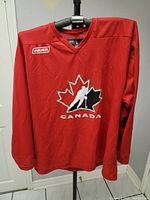 Front view of red Team Canada Bauer hockey jersey with central logo and Bauer branding.