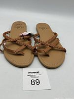 Front angle of the Bobbie Brooks tan braided strap sandals showing sole and strap style with size tag.