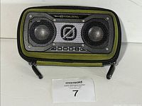 Front view of the portable speaker inside the green and black protective carry case on a white surface with MaxSold lot tag 7 in front.