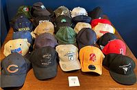 Overview of 29 assorted hats arranged on table, showing multiple colors and logos