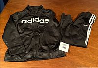 Kids Adidas black zip-up jacket with Adidas logo and matching pants with Adidas logo and stripes, size 7.
