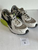 Right and left side view of Nike Air Max Excee sneakers showing white, black, grey, and volt colors with visible signs of wear and dirt on uppers and soles.