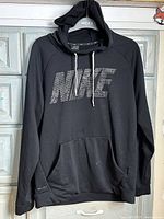 Front view of black Nike hoodie with geometric NIKE logo and kangaroo pocket, hanging on hanger