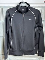 Front view of the black Nike women's full zip jacket with white piping and Nike swoosh logo on chest
