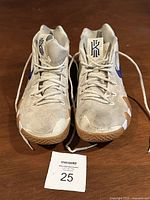 Top and front view of the pair of Nike Kyrie 4 Uncle Drew sneakers showing the toe box, laces, and tongue logos in light beige with navy blue details.