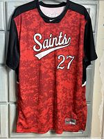 Front view of Nike Saints jersey in red digital camo with black sleeves and shoulders. Shows 'Saints' script and number 27 on front.