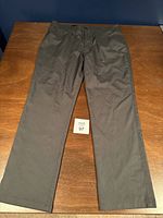 Full view of black PGA Tour golf pants laid flat on a wooden surface.