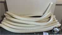 Image displaying several coiled white flexible corrugated pool hoses stacked together.